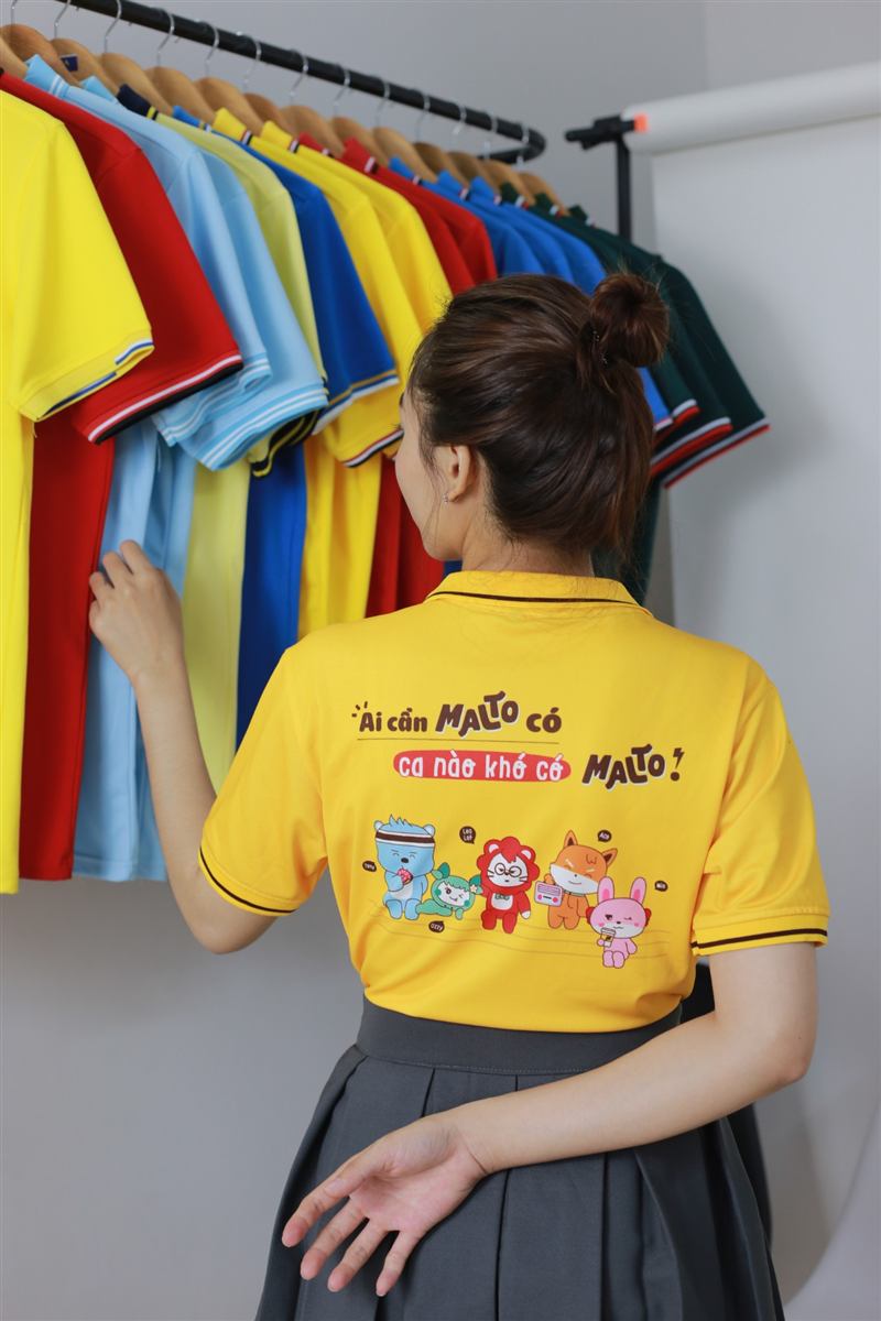 Lưng áo polo vàng in slogan và nhân vật bên giá áo nhiều màu